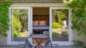 A cozy outdoor bedroom with a bed, a table, and chairs, surrounded by greenery and a wooden deck. - Hotel Ligaro - Jarnac (Jarnac)