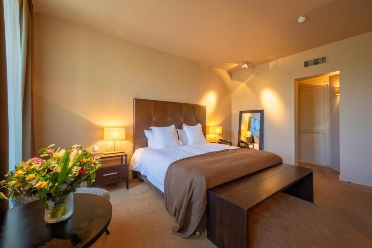 Ein Hotelzimmer mit Bett, Nachttischen, einer Bank, einem Blumenstrauß und einem Spiegel.