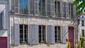 A two-story building with multiple windows and shutters, a red door, and potted plants on the windowsills. - Hotel Ligaro - Jarnac (Jarnac)
