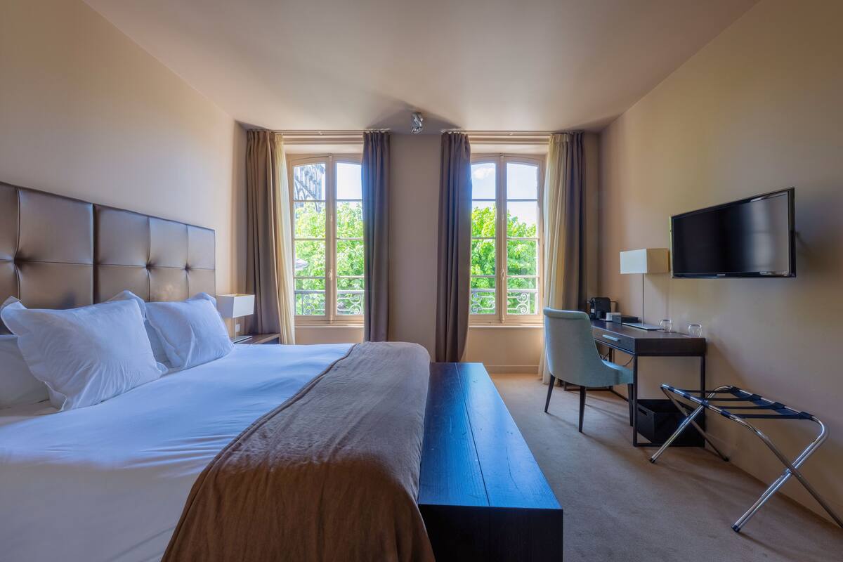 Habitación de hotel con una cama grande, un escritorio, una silla, un televisor y una ventana con cortinas.