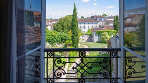 A view from a window with ornate iron railings, overlooking a courtyard with a pathway, a tall tree, and a building with a tiled roof. - Hotel Ligaro - Jarnac (Jarnac)