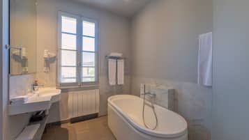Un bagno moderno con una vasca freestanding, un mobile lavabo con specchio e una finestra che permette l'illuminazione naturale.