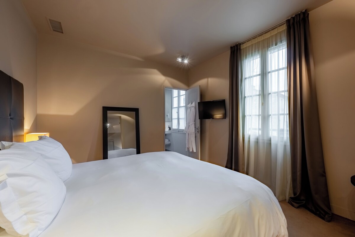 A hotel room with a large bed, a flat-screen TV mounted on the wall, and a window with curtains.