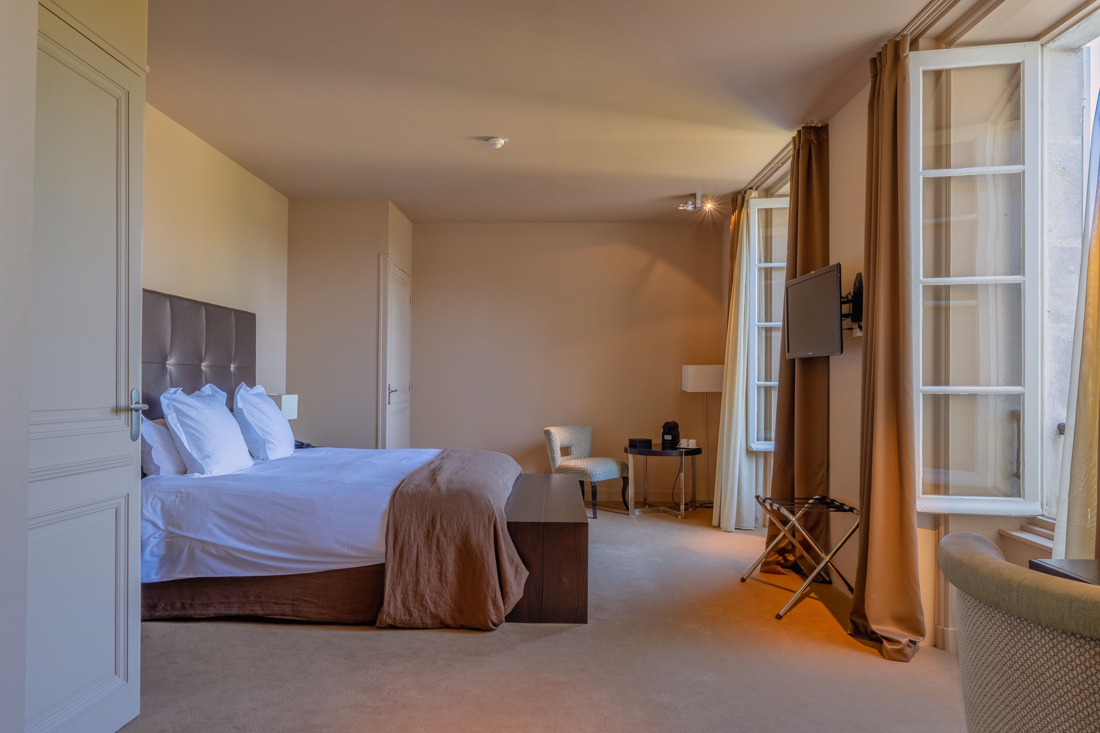Habitación de hotel con cama, sillón, escritorio, televisor de pantalla plana y ventana con cortinas.