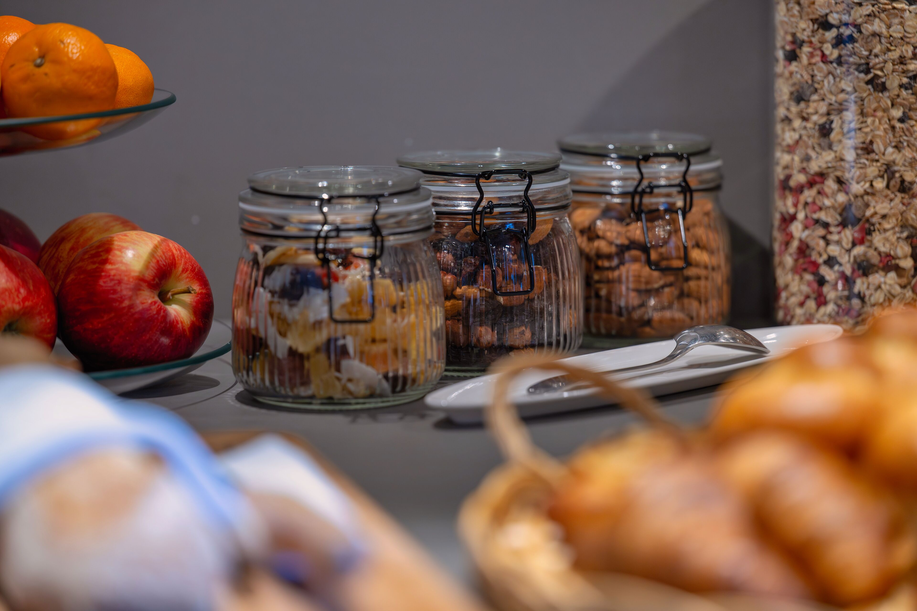 Una mesa de buffet con diferentes alimentos, incluyendo manzanas, naranjas y frascos con frutos secos y semillas.