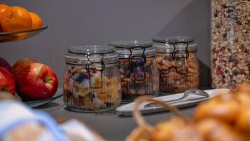 Una mesa de buffet con diferentes alimentos, incluyendo manzanas, naranjas y frascos con frutos secos y semillas.