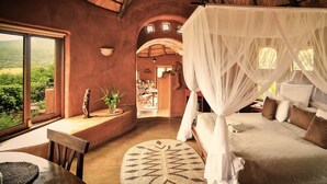 A bedroom with a canopy bed, a view of the outdoors, a dining area, and a small statue. - Leshiba Wilderness (Louis Trichardt)