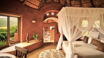 A bedroom with a canopy bed, a view of the outdoors, a dining area, and a small statue.