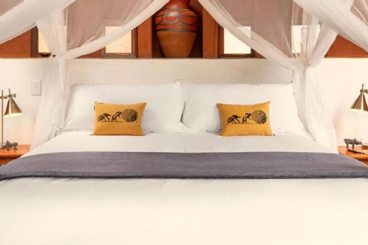 A bed with white linens and two decorative pillows, a bedside lamp, and a decorative vase on the nightstand.