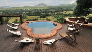 A hot tub surrounded by wooden deck chairs on a wooden deck with a scenic view of hills and trees. - Leshiba Wilderness (Louis Trichardt)