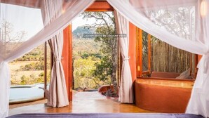 A bedroom with a view of a mountainous landscape, a wooden floor, and a bed with a purple bedspread. - Leshiba Wilderness (Louis Trichardt)