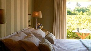 Camera da letto con un letto grande, una lampada da comodino, una finestra con tende e vista su del verde all'esterno.