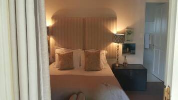 A bedroom with a large bed, a nightstand, a lamp, and a door.