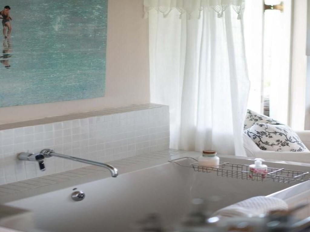 A bathroom with a bathtub, a shower, a towel rack, and a window with curtains.
