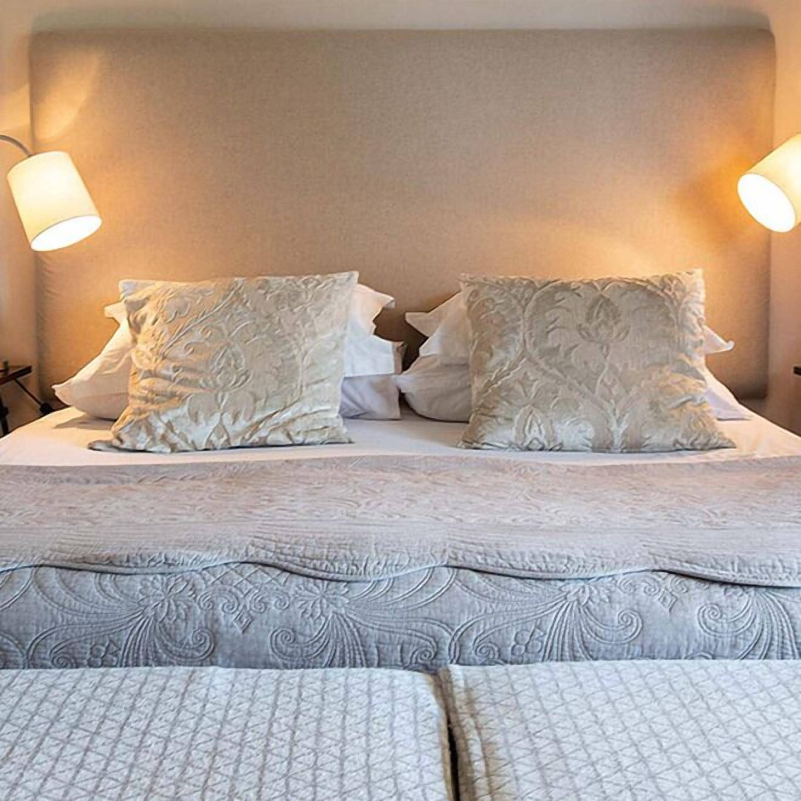 Een opgemaakt bed met een beddekleed met dessin en twee decoratieve kussens.
