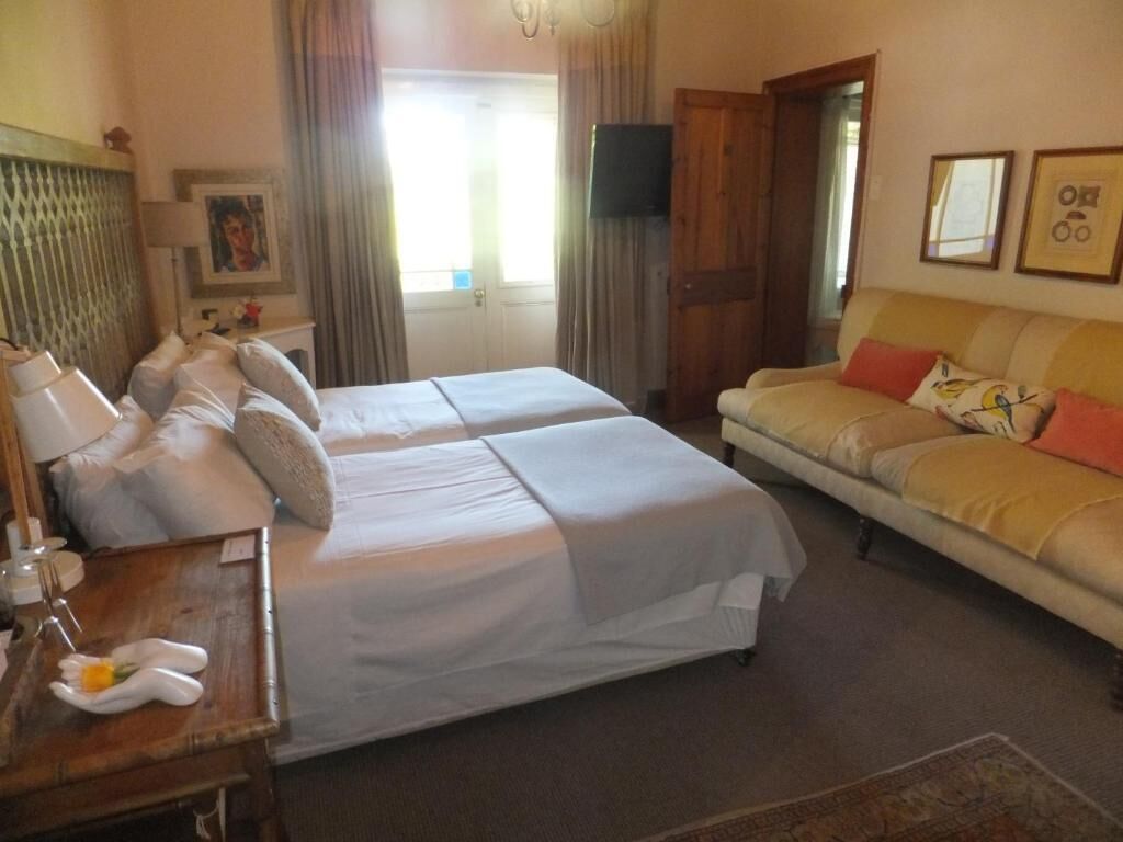 A hotel room with two beds, a sofa, a wooden nightstand, a TV, and a window with curtains.