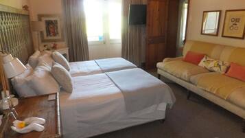 A hotel room with two beds, a sofa, a wooden nightstand, a TV, and a window with curtains.