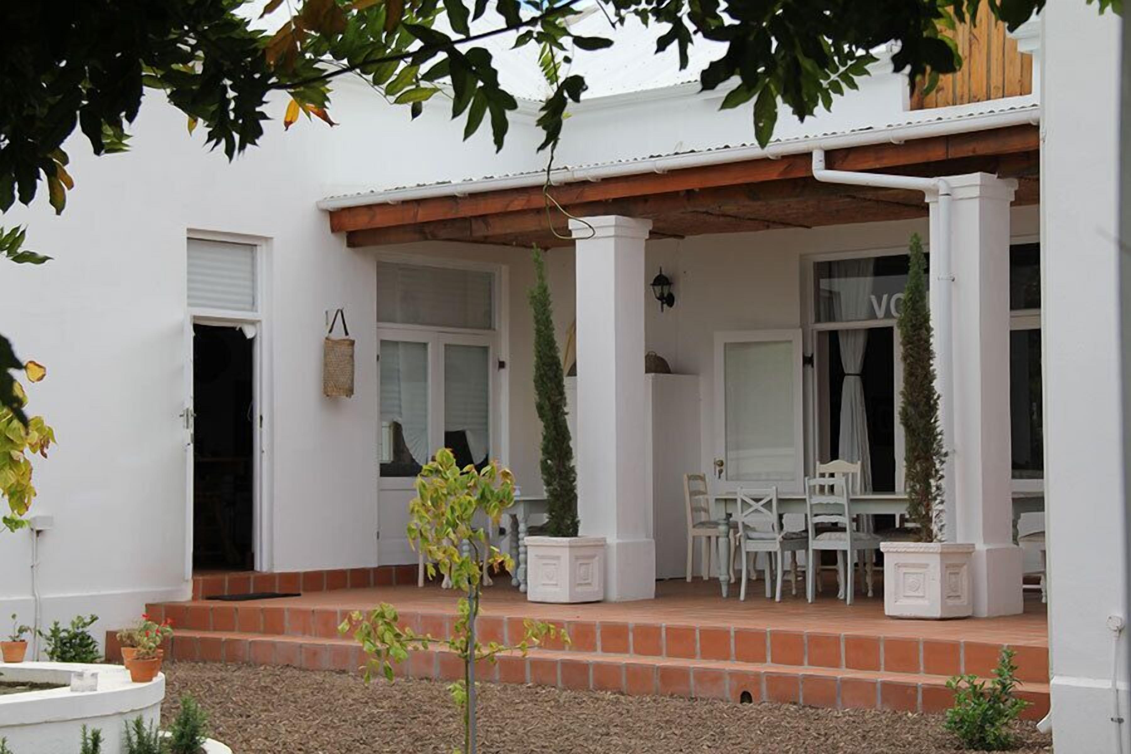 A white building with a covered porch, outdoor seating, and potted plants.