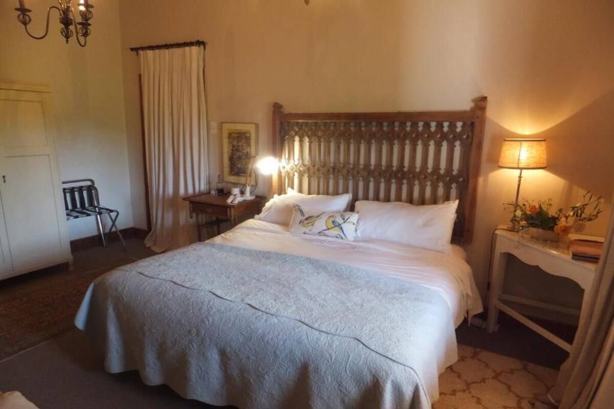 A neatly arranged hotel room with a large bed, a bedside table with a lamp, a chair, and a desk.