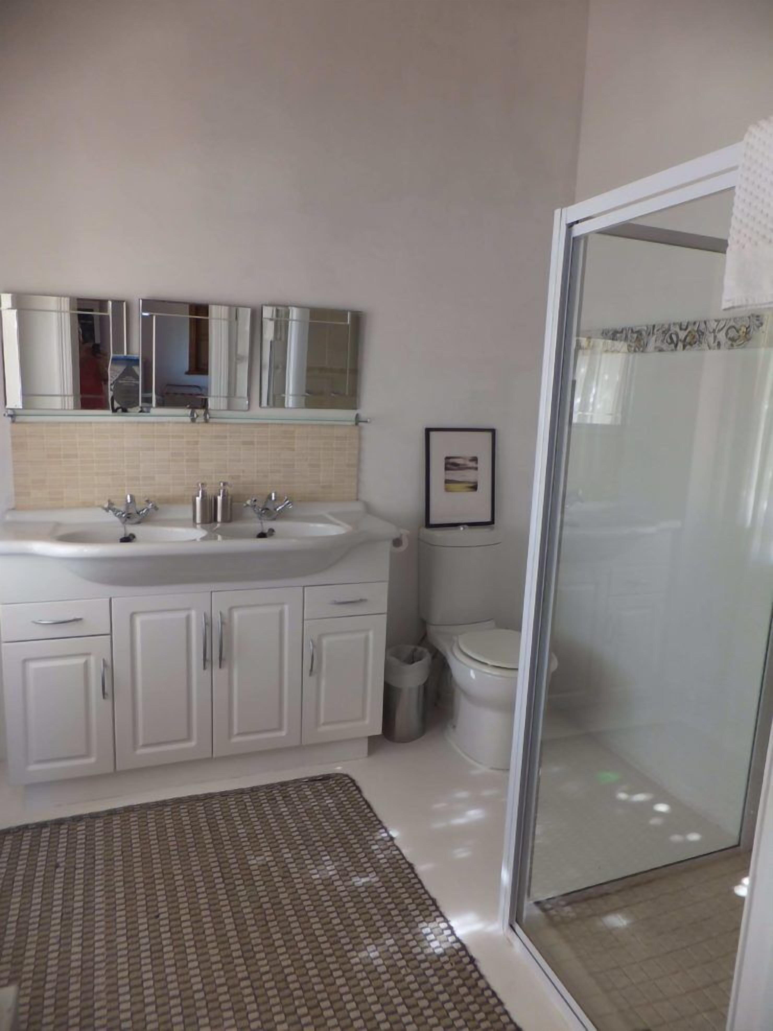 Une salle de bain avec un double vasque, des toilettes et une douche à parois de verre.