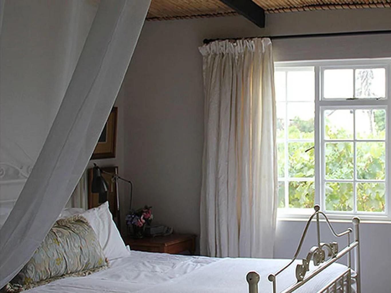 Une chambre à coucher avec un lit, une fenêtre avec des rideaux et une table de chevet avec une lampe.