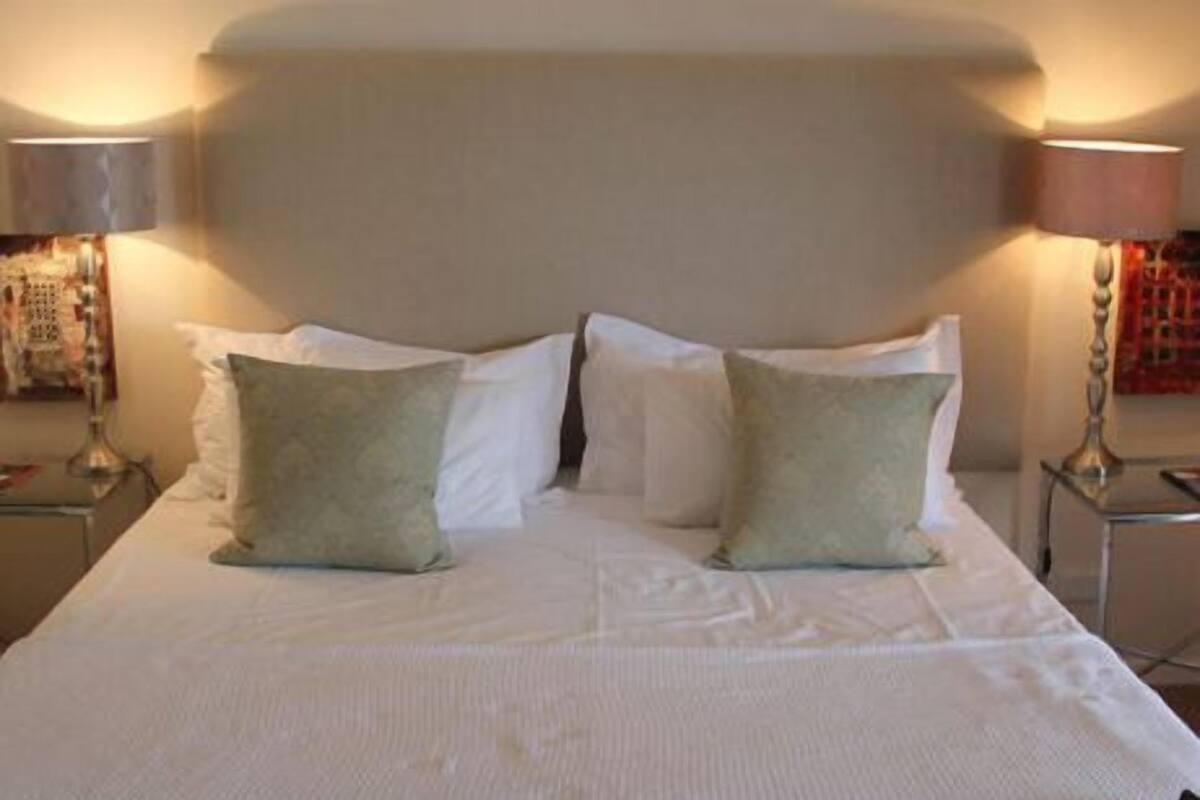 A neatly made bed with white linens and two green pillows.