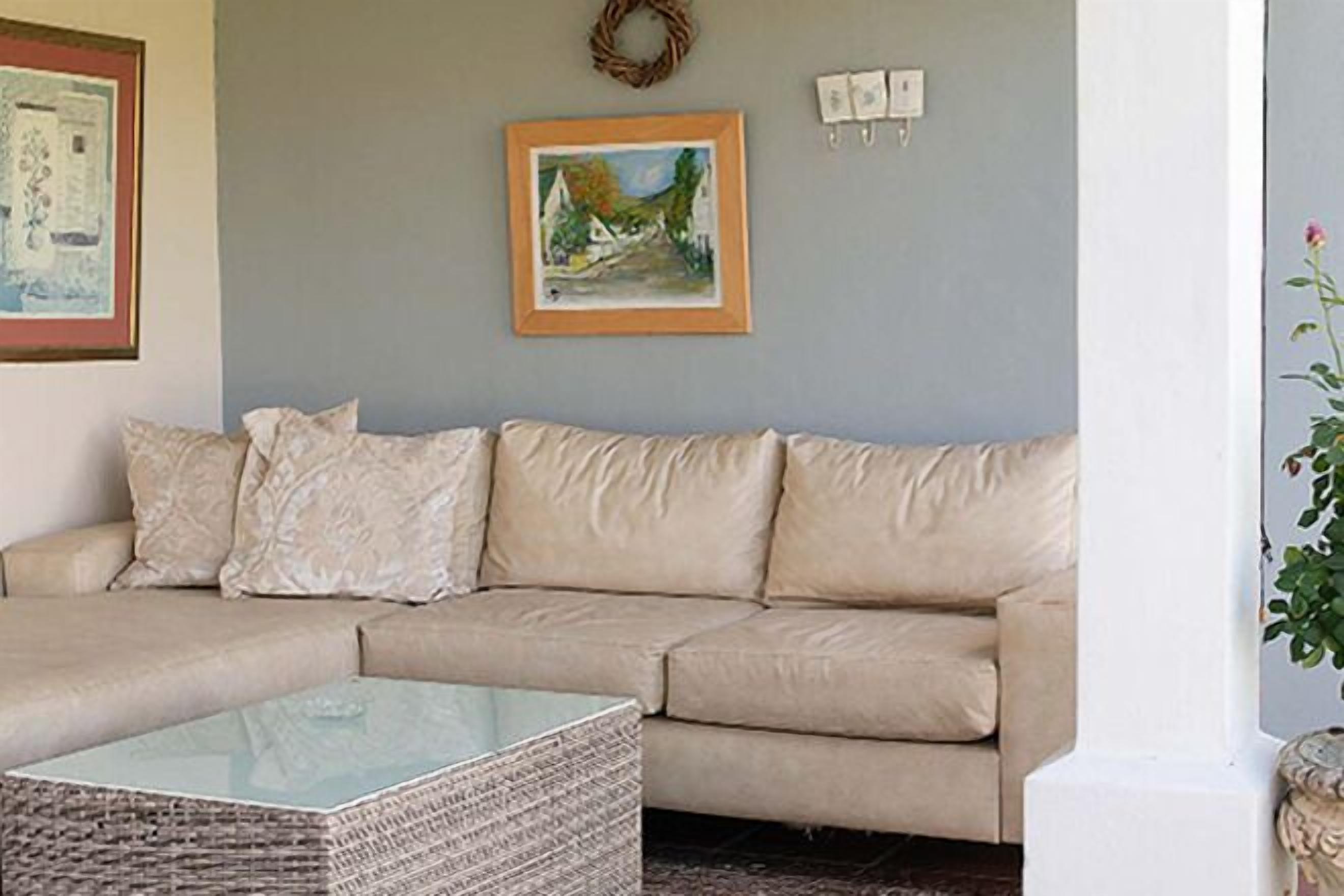 A beige sofa with a glass coffee table in front, a framed painting on the wall, and a wreath above the sofa.