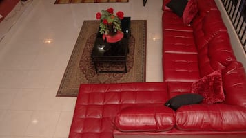 Un sofá de cuero rojo, una mesa de centro negra con un centro de mesa floral y una alfombra estampada en una sala de estar moderna.