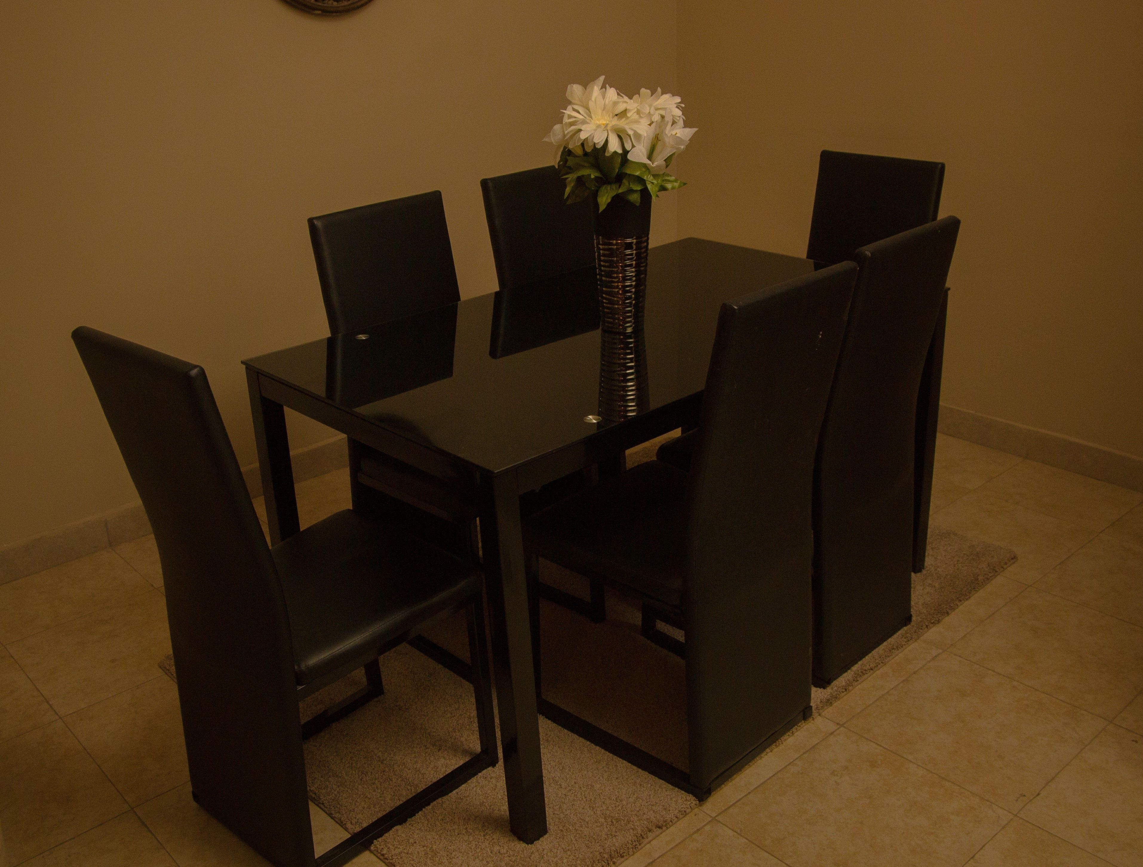 Una mesa de comedor con cuatro sillas, un jarrón con flores blancas y un reloj en la pared.