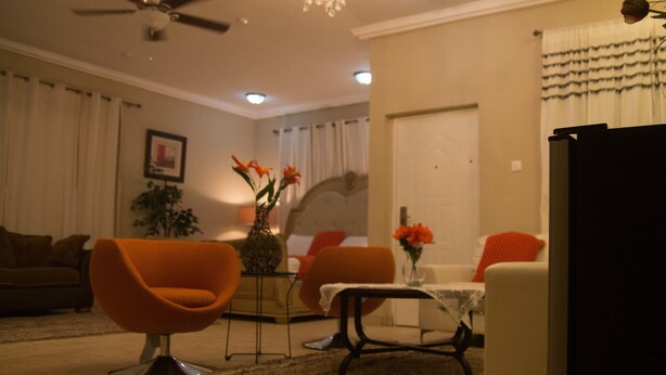 A living room with orange chairs, a coffee table, and a ceiling fan. - Appiah's Royal Suites (Accra)