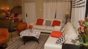 A living room with a sofa, armchairs, a coffee table, and a door. - Appiah's Royal Suites (Accra)