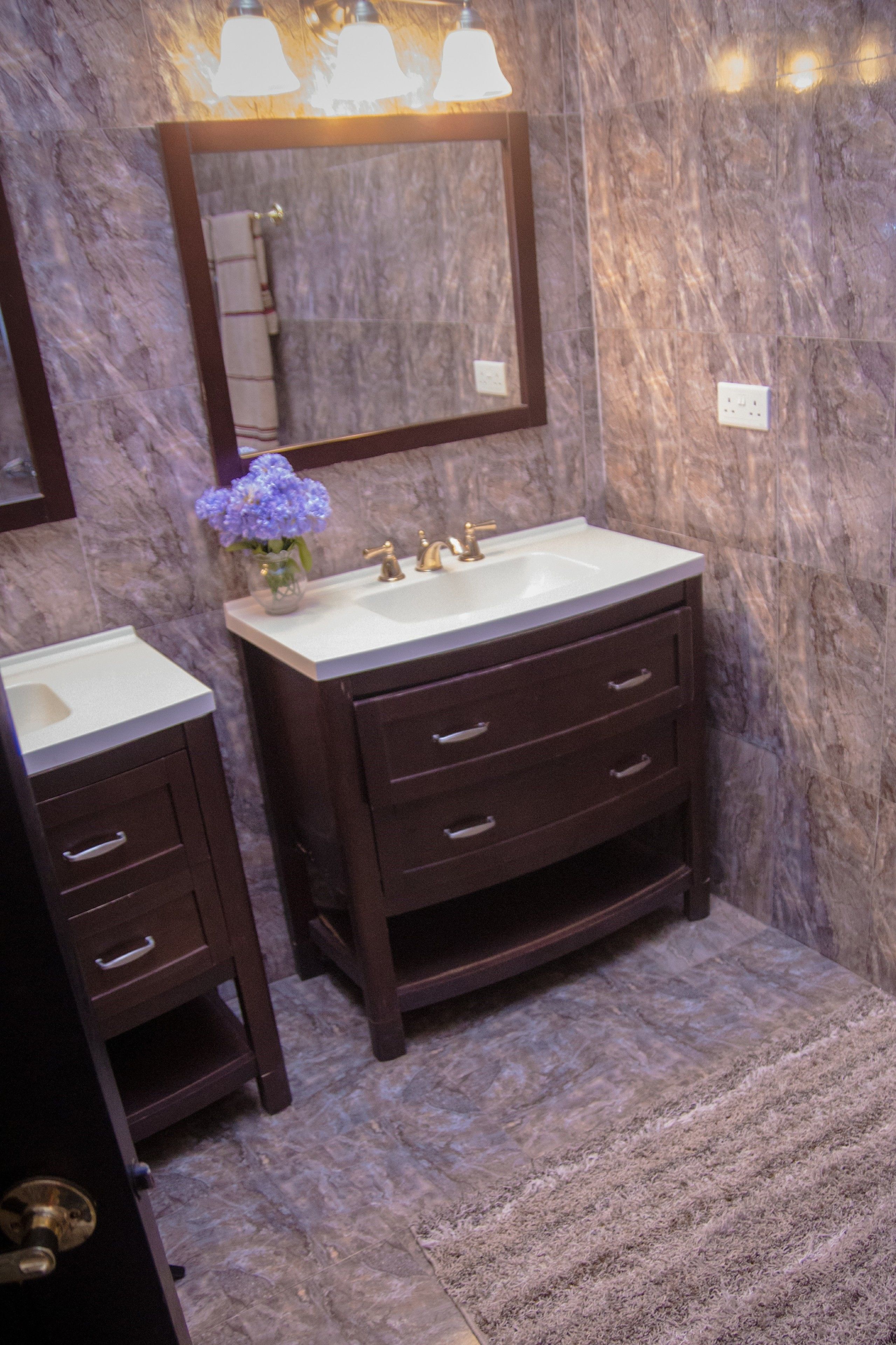 A bathroom with a marble wall, a sink with a mirror, and a towel rack.