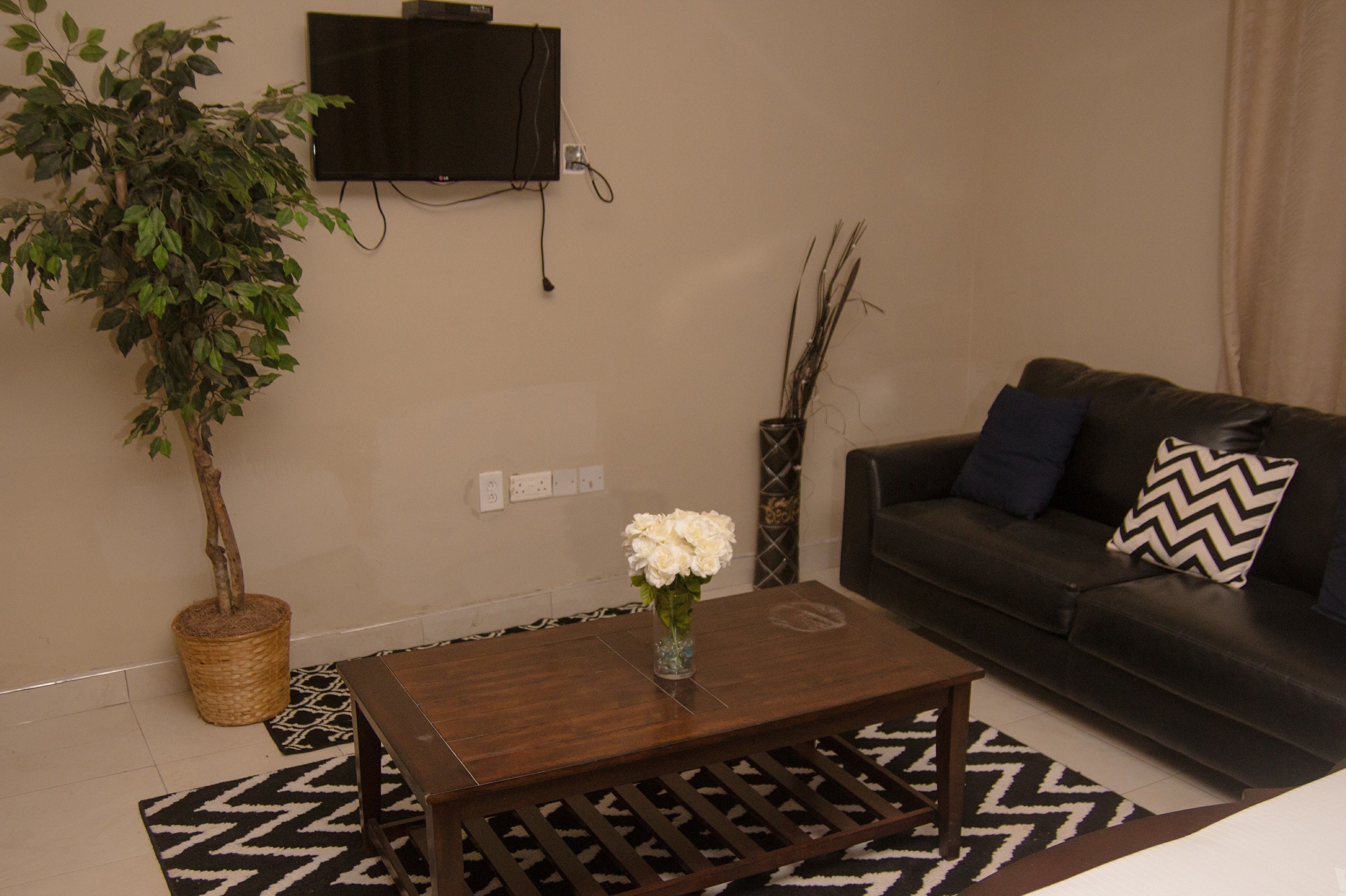 Ein Wohnzimmer mit einem dunkelbraunen Ledersofa, einem Couchtisch aus Holz mit einer Vase voller weißer Blumen, einer Topfpflanze und einem schwarz-weißen Teppich.