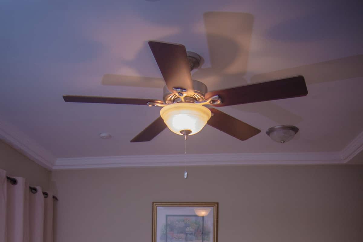 Habitación de hotel con cama, ventilador de techo, un cuadro en la pared y dos lámparas de noche.