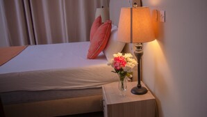 A neatly made bed with a red pillow, a bedside table with a lamp and a vase of flowers, and a wall socket. - Appiah's Royal Suites (Accra)