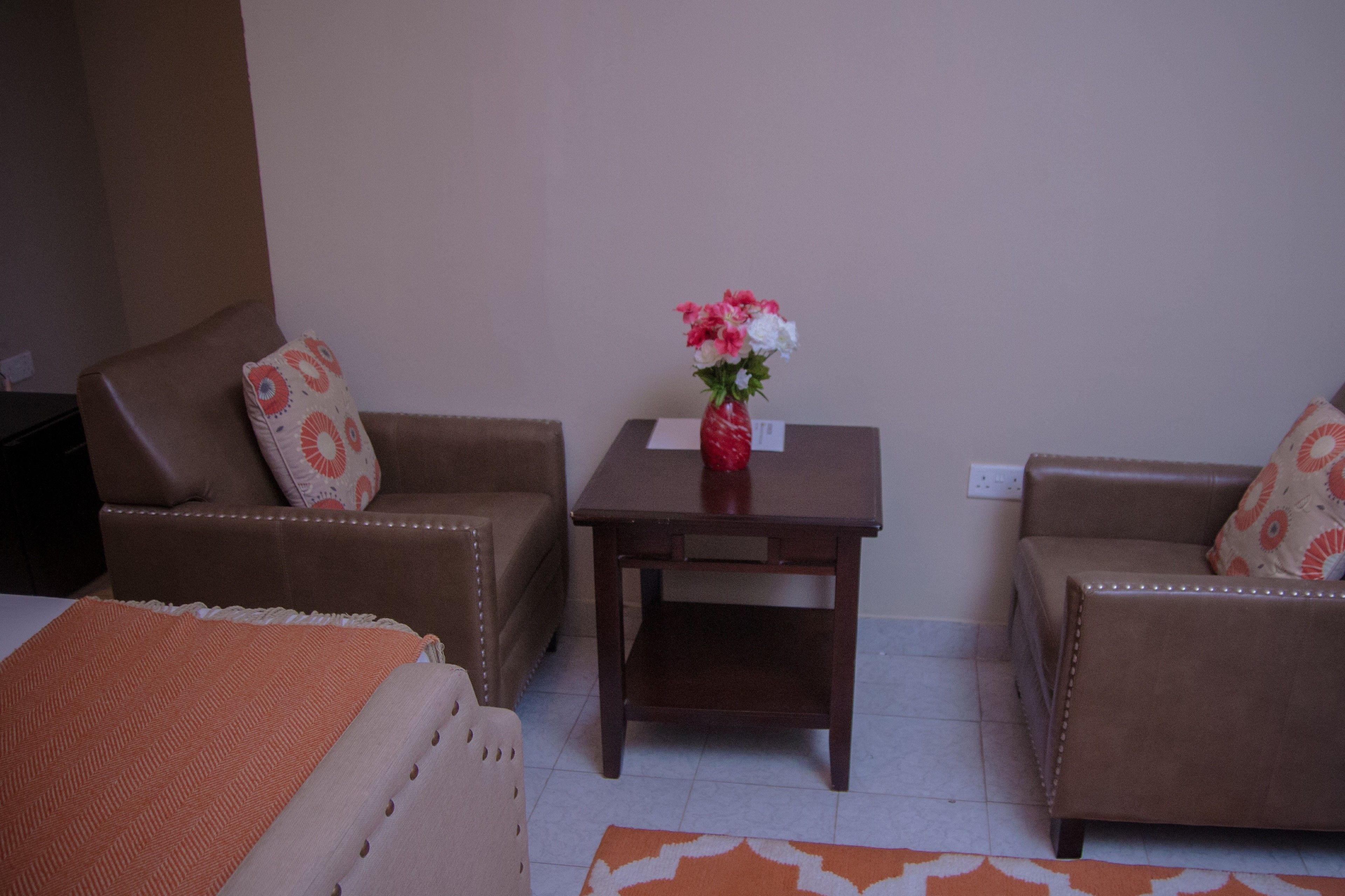 Una habitación con dos sofás de cuero marrón, una mesita de madera con un jarrón de flores y una cama con una manta naranja.