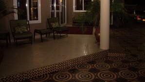 A covered outdoor seating area with chairs and a table, surrounded by potted plants and a patterned floor. - Appiah's Royal Suites (Accra)
