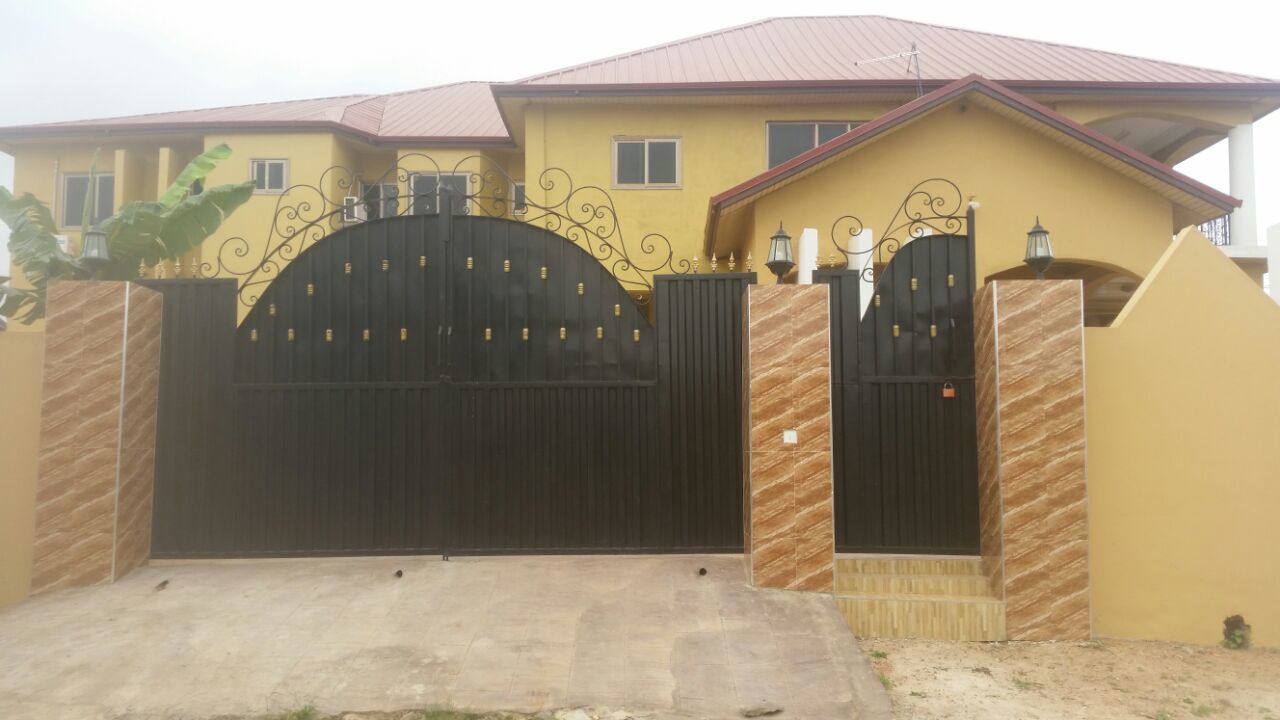 A gated residential property with a yellow facade, a black gate, and a red roof.