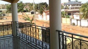A spacious balcony with ornate metal railings, a tiled floor, and a view of a residential area with buildings and greenery.