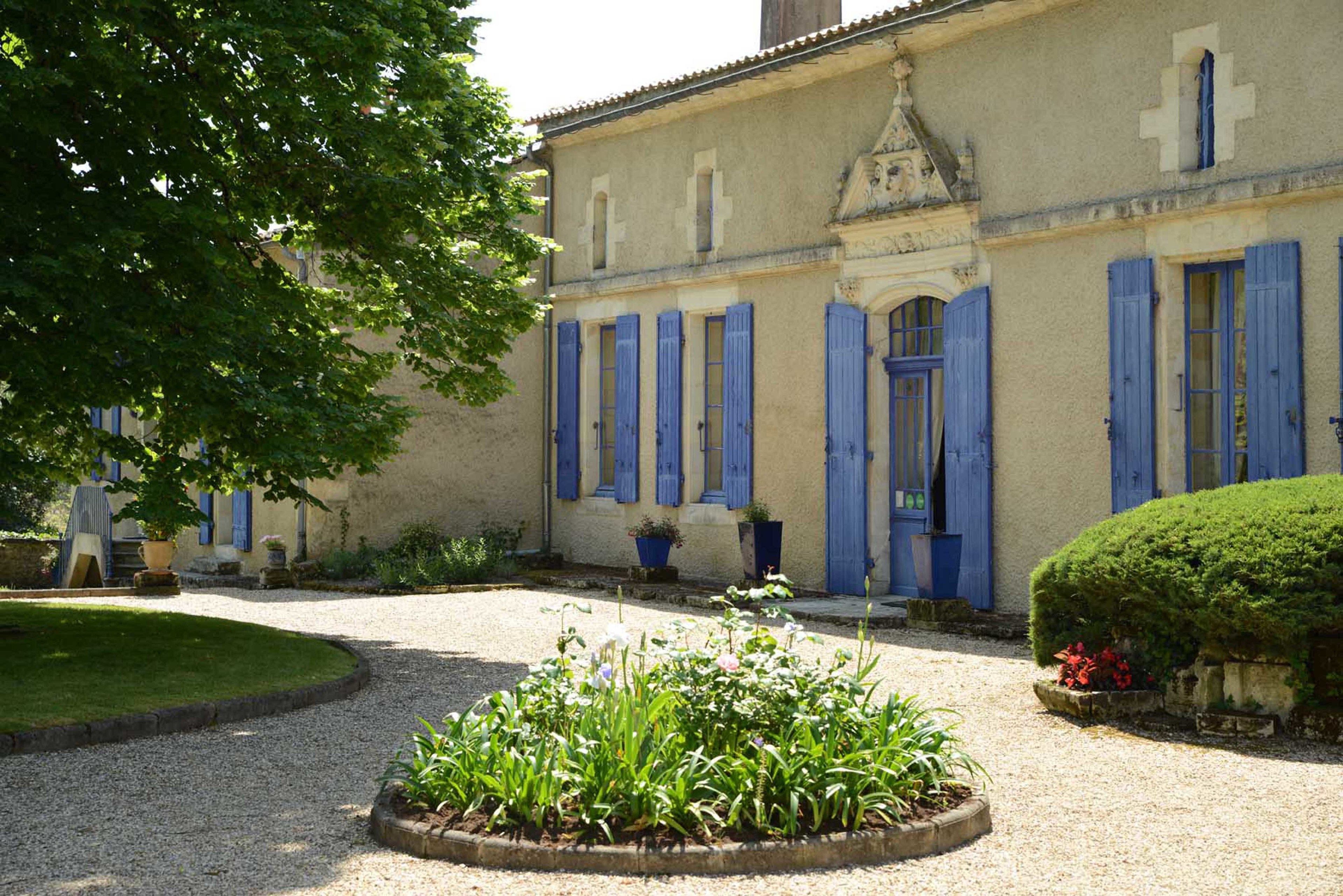 Ein Gebäude mit blauen Fensterläden und ein Garten mit Kieswegen und Pflanzen.