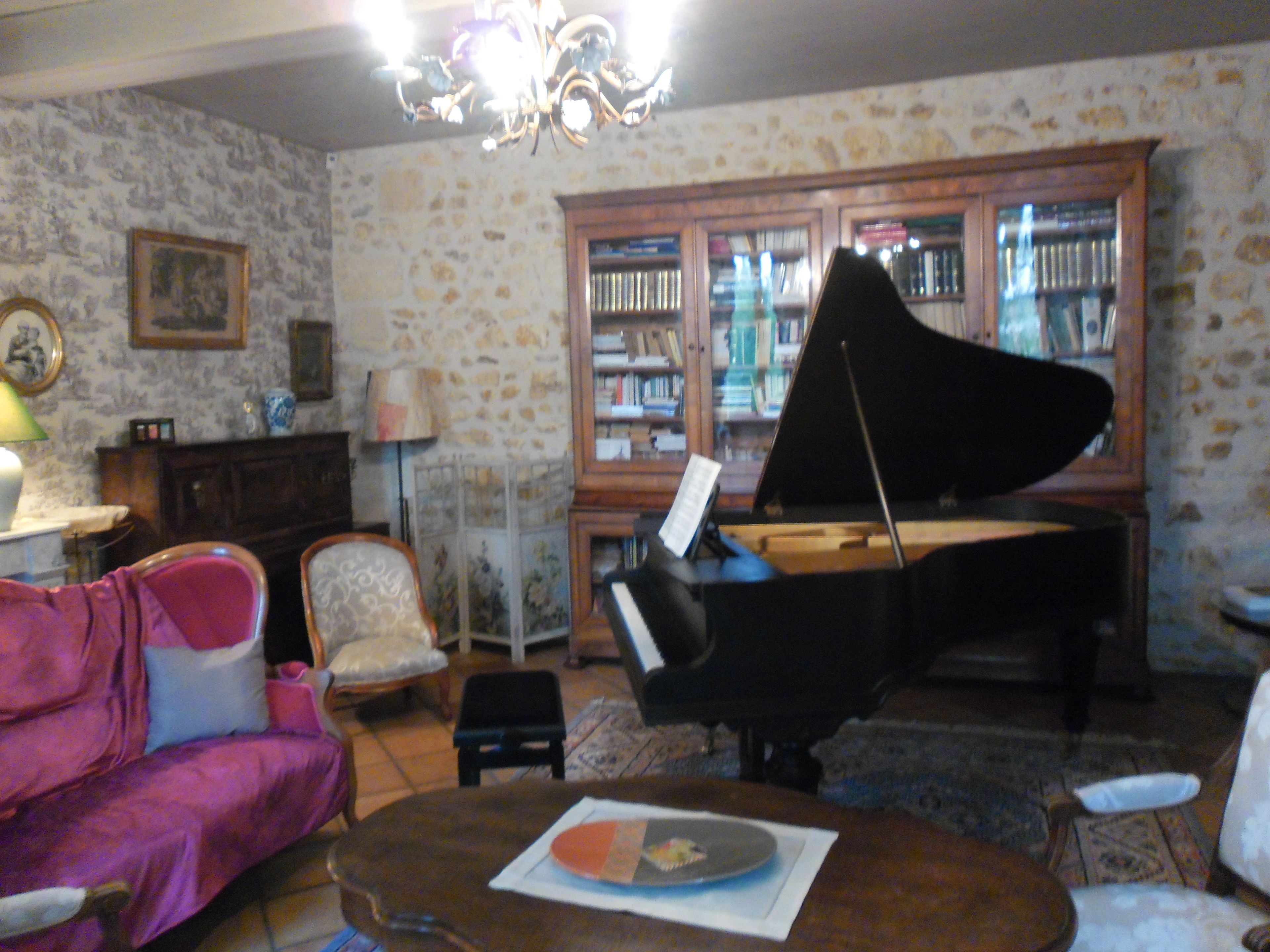 A living room with a grand piano, a pink sofa, and a bookshelf filled with books.
