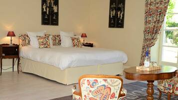 A bedroom with a large bed, two bedside tables with lamps, a round wooden table, and patterned chairs.