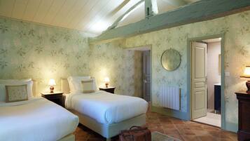 Un dormitorio con dos camas, techo de madera, papel tapiz floral y una puerta que da a otra habitación.