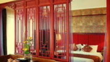 A traditional room with a bed, a wooden sofa, and a decorative screen.