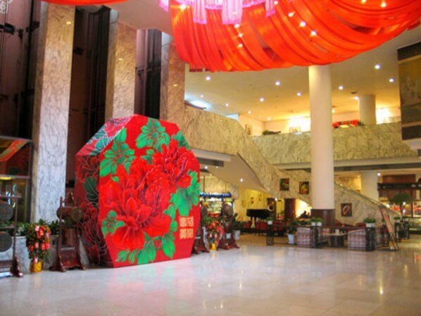 Een ruime binnenruimte met een grote decoratieve bloemstructuur, marmeren kolommen en een roltrap.