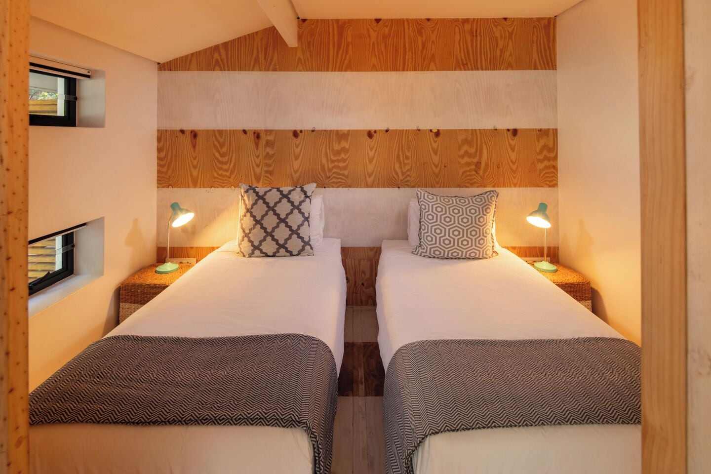 Une chambre avec deux lits, chacun recouvert d’une couvre-lit à motifs et agrémenté de coussins assortis. On y trouve des tables de chevet avec des lampes, et les murs sont recouverts de lambris en bois.
