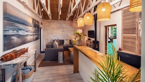 A modern interior with exposed wooden beams, a brick wall, a wooden reception desk, a grey sofa, and a large fish decoration. - The Bungalow  (Plettenberg Bay)