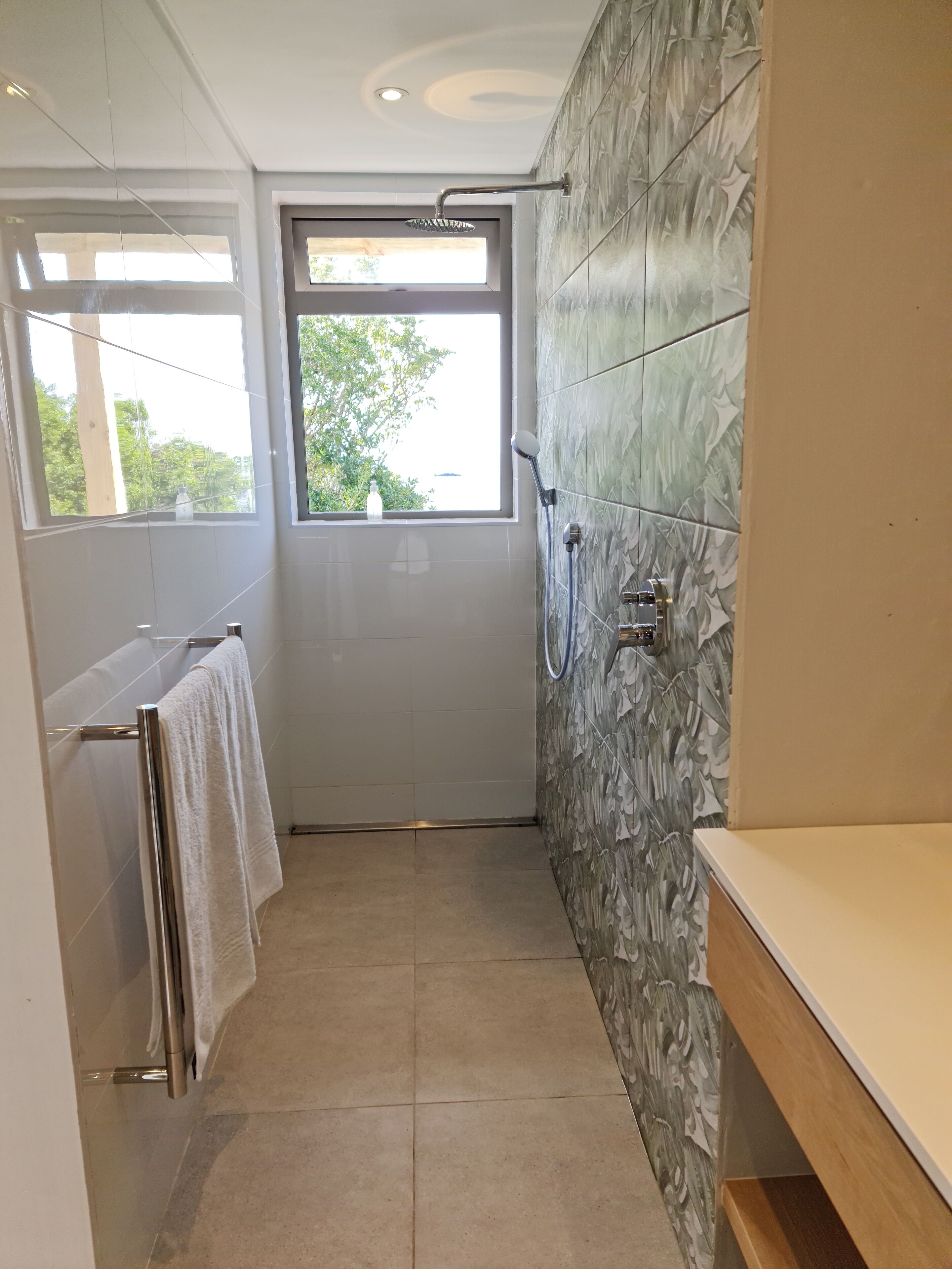 A modern bathroom with a shower, a window, and a towel rack.