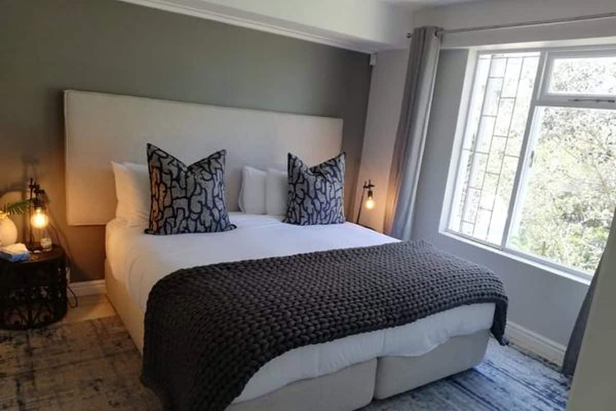 Quarto com uma cama grande, duas luminárias de cabeceira, mesa de cabeceira e janela com vista para árvores.