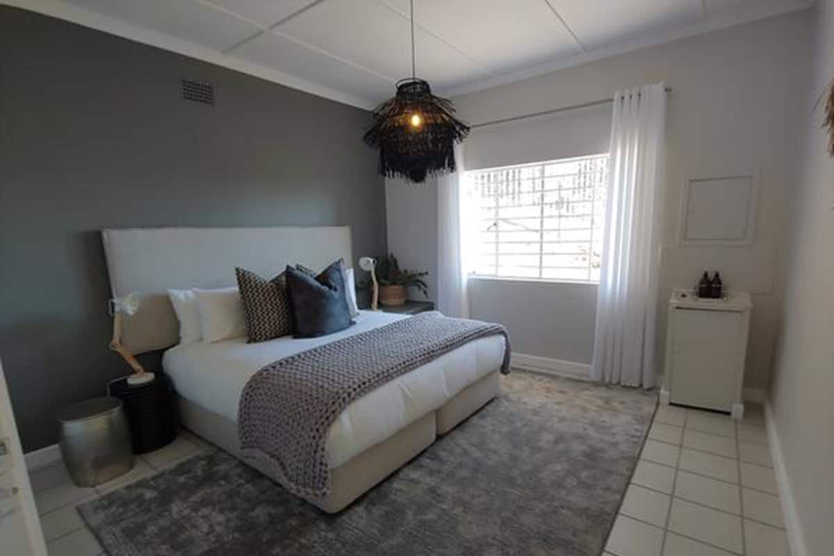 Quarto com cama grande, mesa de cabeceira, abajur, pequeno armário e janela com cortinas.